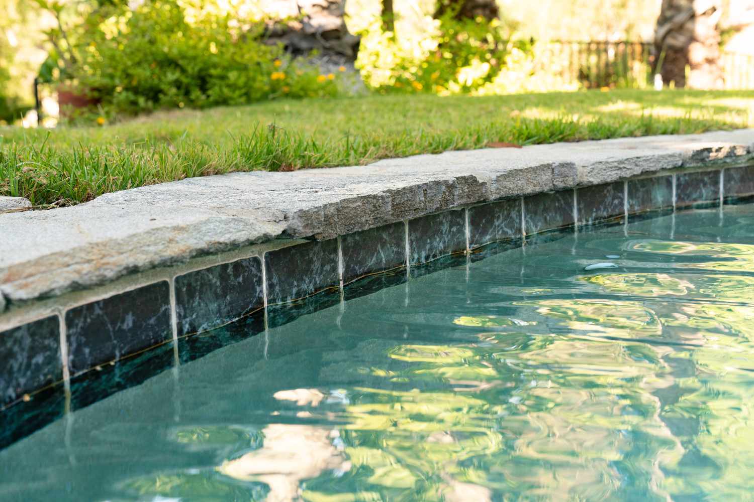 Azulejos azuis escuros revestindo a piscina com uma passarela de pedras ao lado do gramado