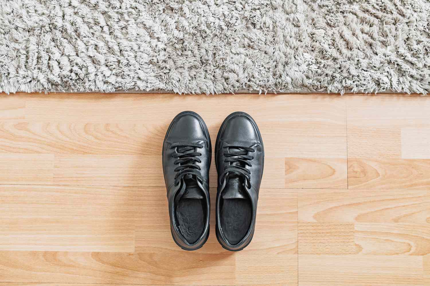 Zapatos negros colocados junto a alfombra mullida sobre suelo de madera