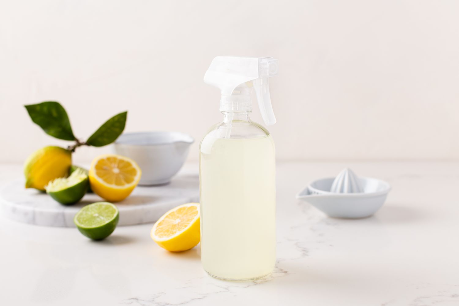 Zitronen-Limetten-Reinigungslösung in klarer Sprühflasche neben geschnittenen Zitronen und Limetten