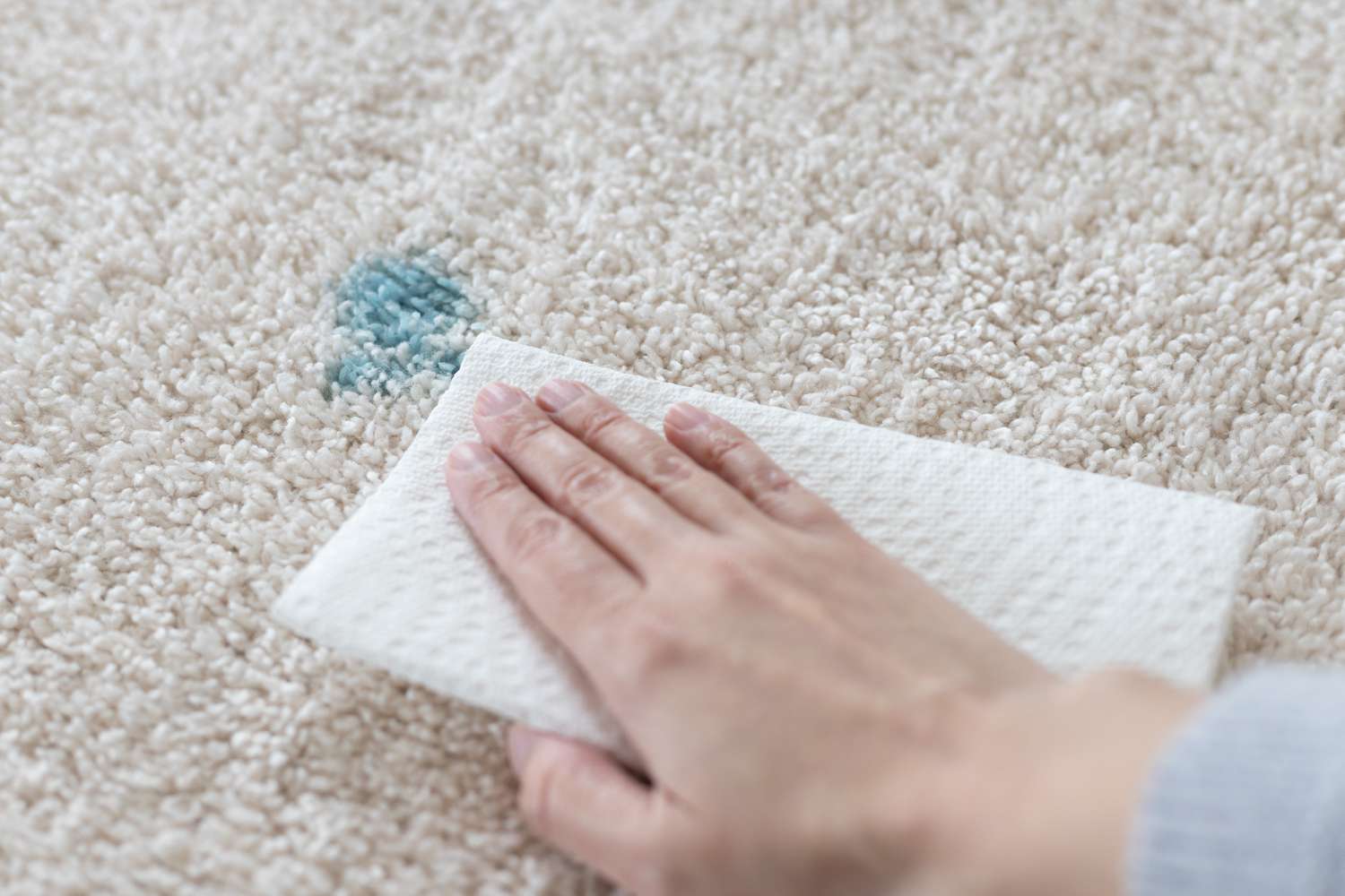 Mit blauer Ostereierfarbe befleckter Teppich, abgetupft mit weißem Papierhandtuch