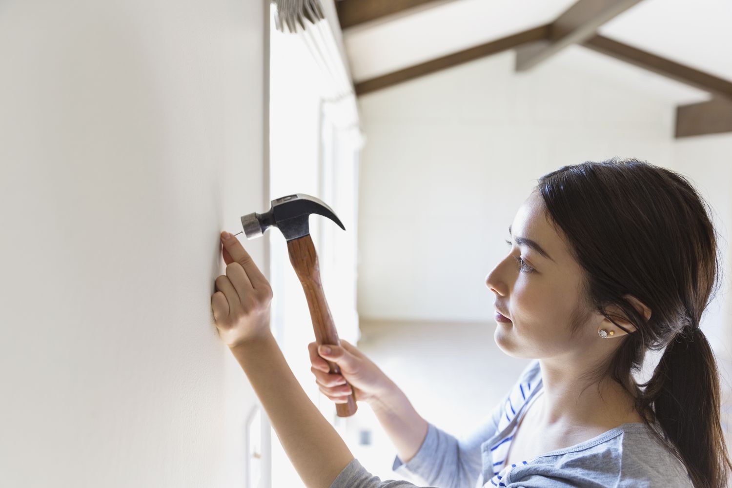 Junge Frau hämmert zu Hause einen Nagel in die Wand