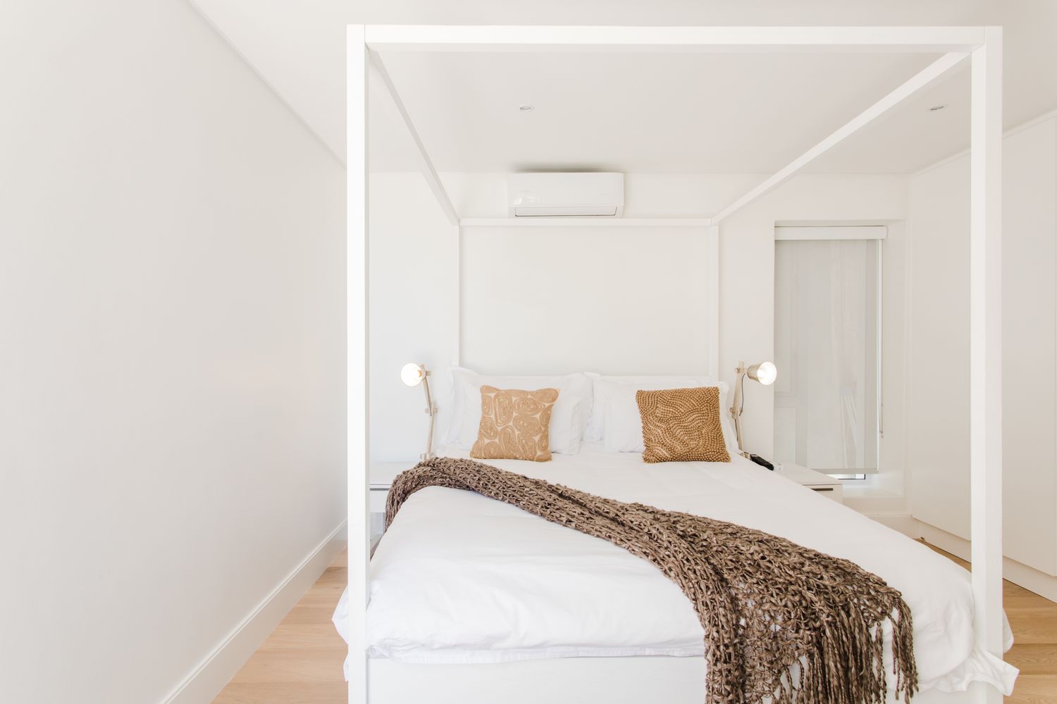 Cama de dossel branca de tamanho normal com dois travesseiros marrons e cobertor em um quarto branco