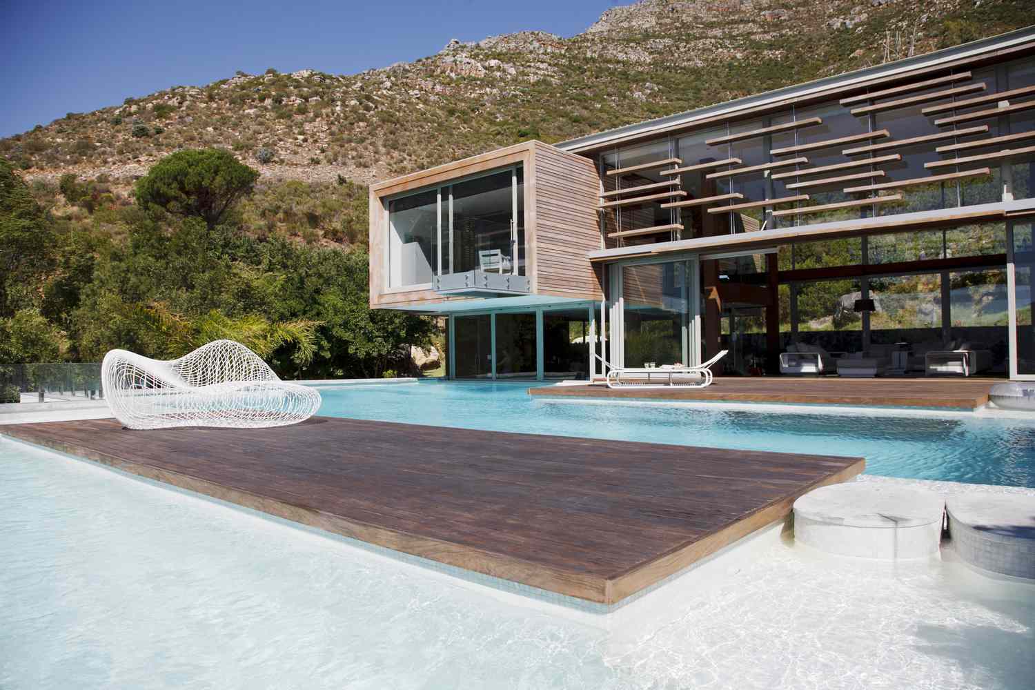 Uma piscina moderna com uma casa moderna perto das montanhas.