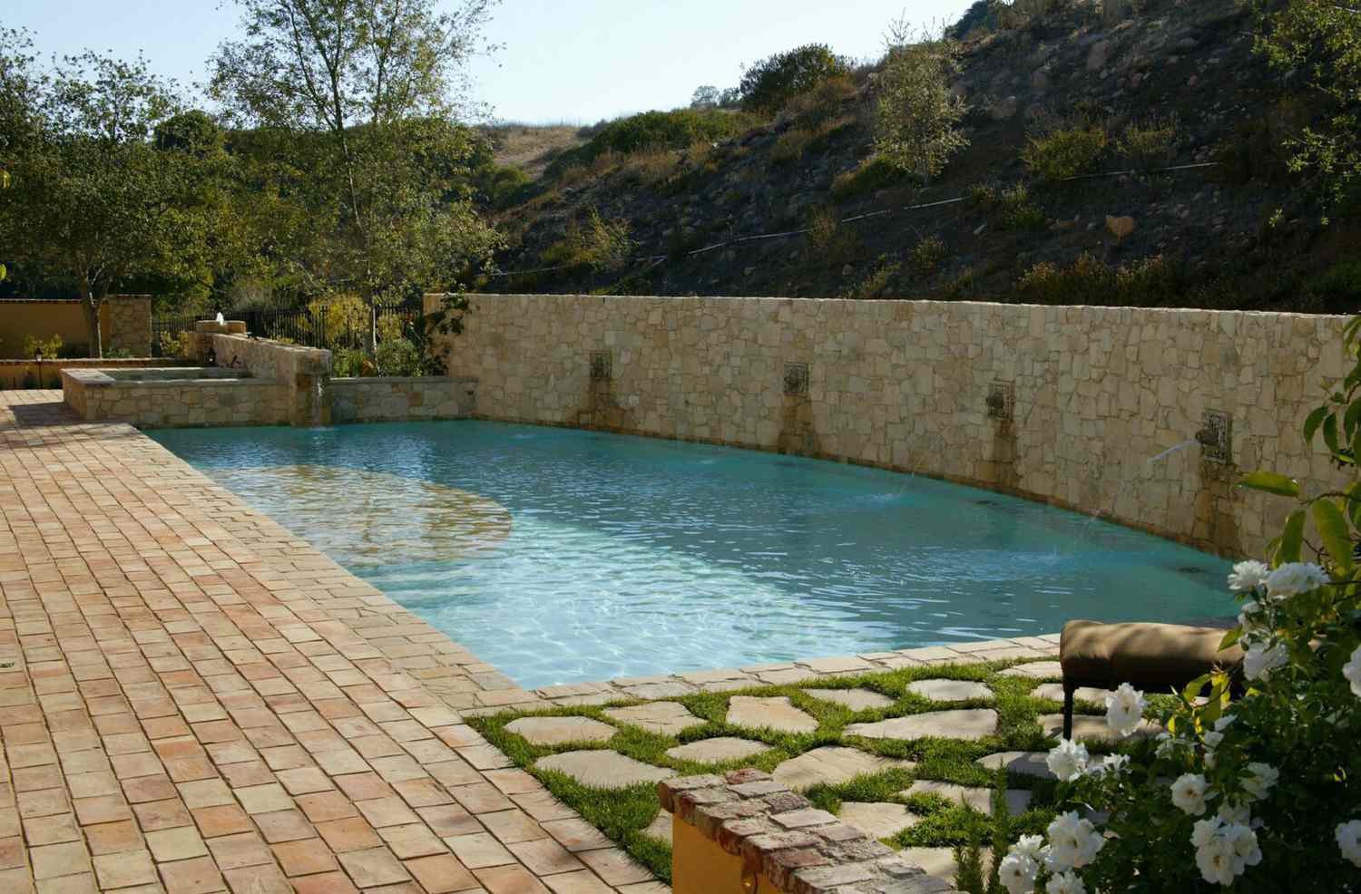 Mediterraner Pool mit beiger Kachelwand und grasbewachsenem Steinweg.