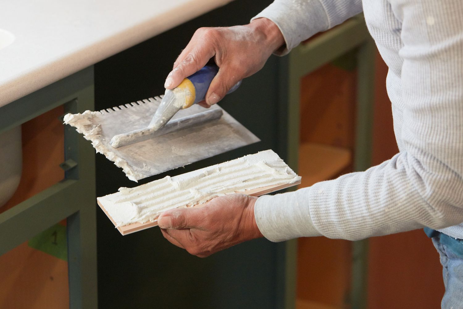 White tile mastic being scraped and applied to back of tile by hand