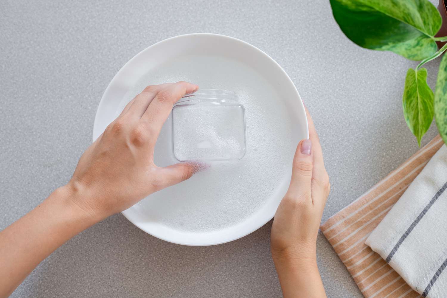 Recipiente de cristal sumergido en un bol blanco con agua jabonosa para eliminar los restos de pegatina