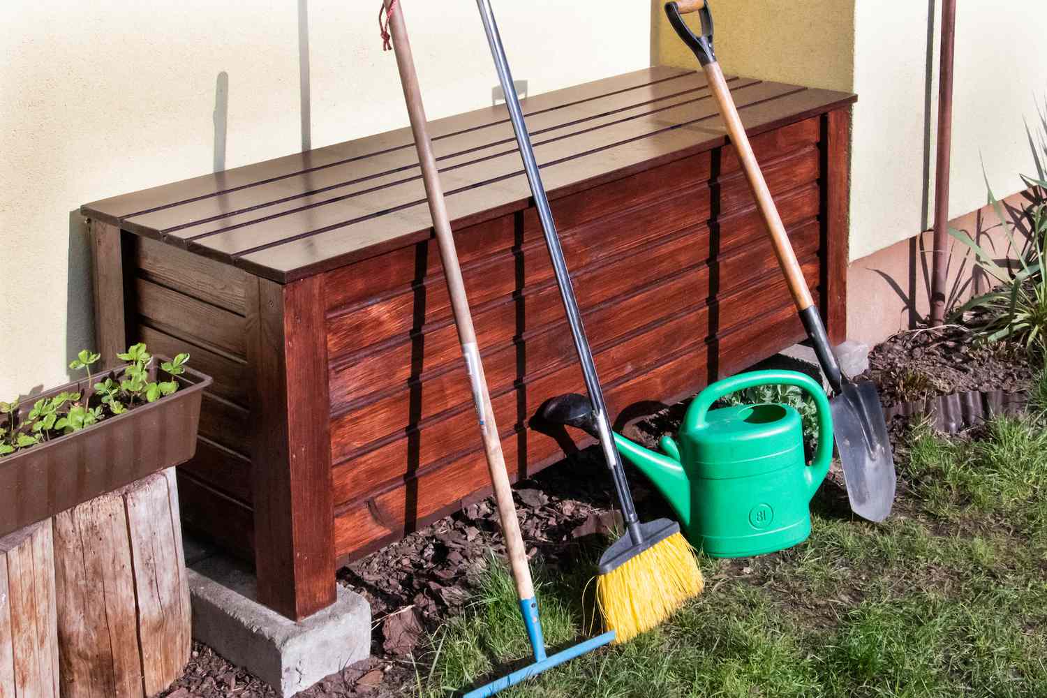 Baúl de herramientas de madera con herramientas de jardín apoyadas y regadera verde