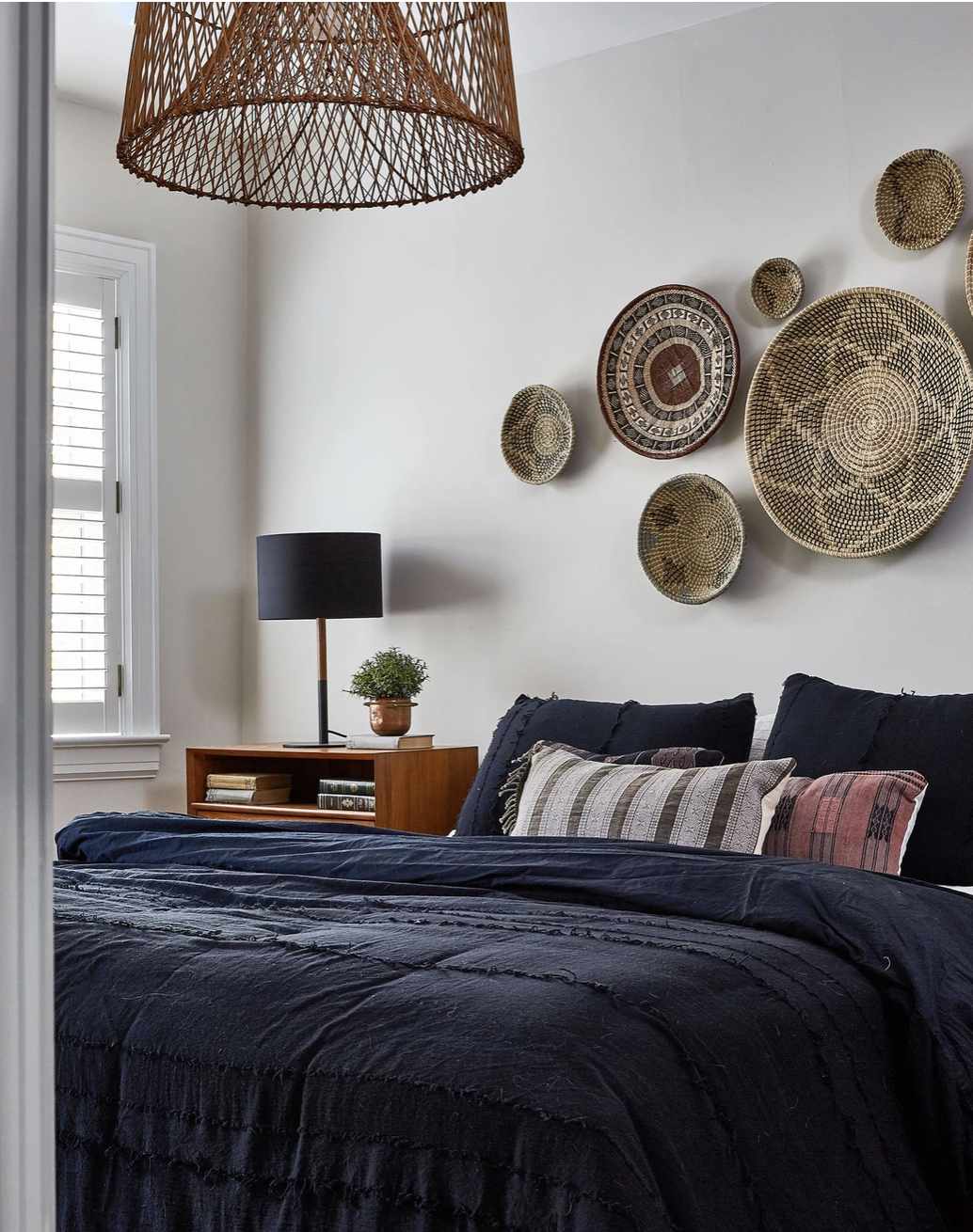 bedroom with navy comforter and gallery wall of baskets hanging above bed