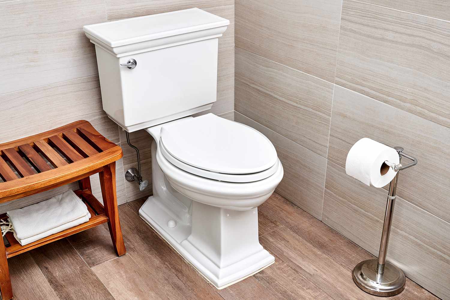 Weiße Toilette neben einer Holzbank mit gefaltetem Handtuch und Toilettenpapierständer