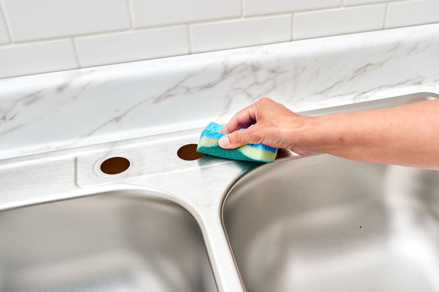 Trous de robinet vides nettoyés avec une éponge bleue sur l'évier de cuisine