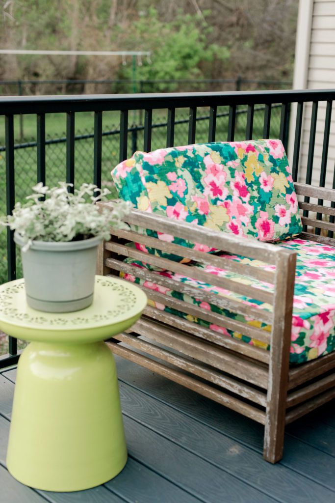 Ein Terrassenstuhl mit geblümtem Stoff neben einem gelben Pflanzenständer.