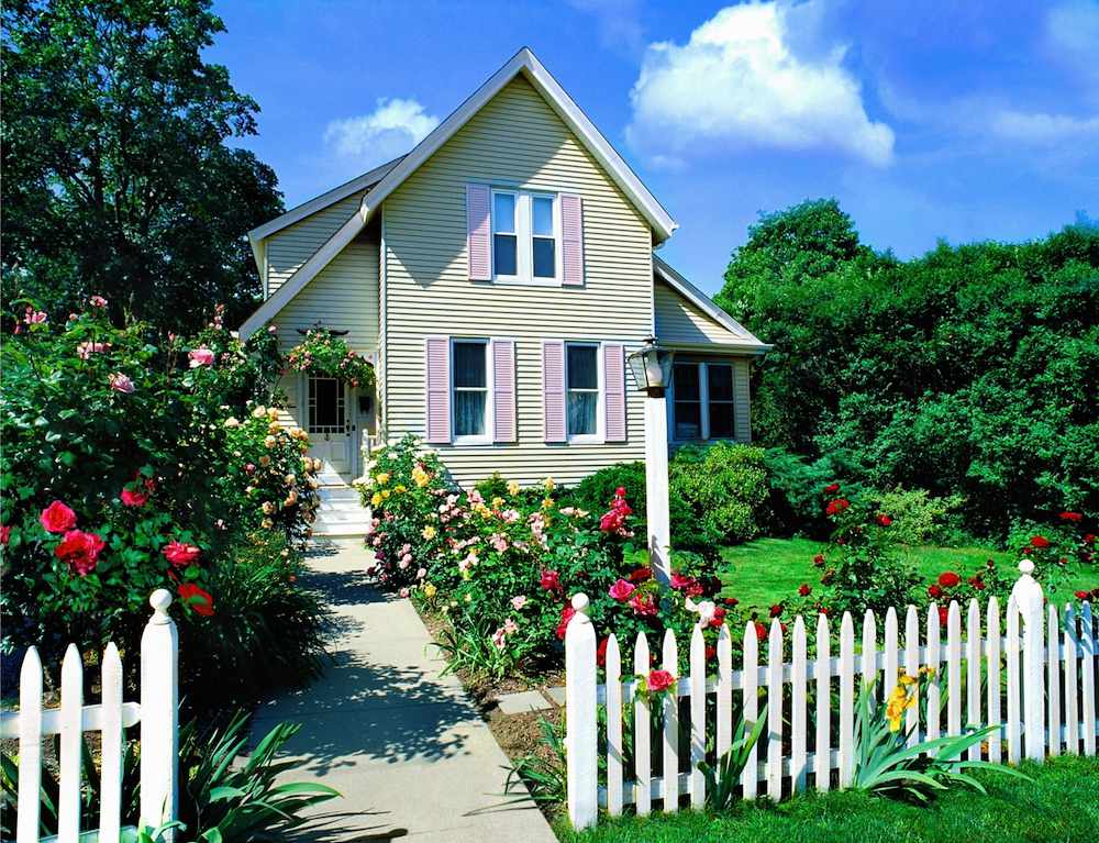 weißer Lattenzaun mit Blumen und Büschen vor dem Haus