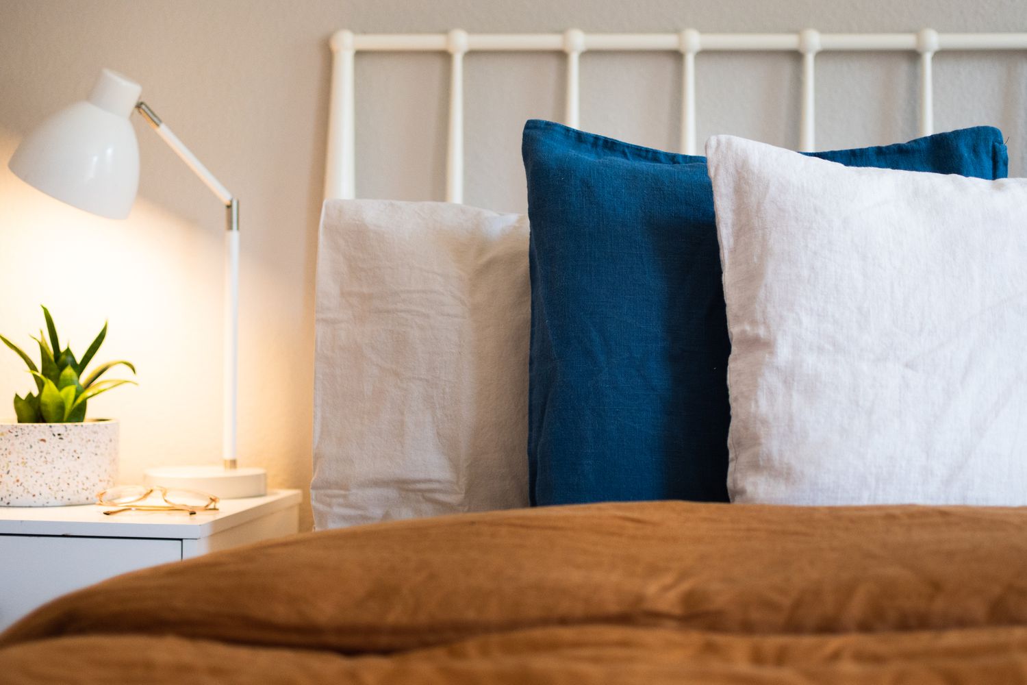 Kissen mit blauen und cremefarbenen Leinenbezügen neben Nachttisch mit Lampe