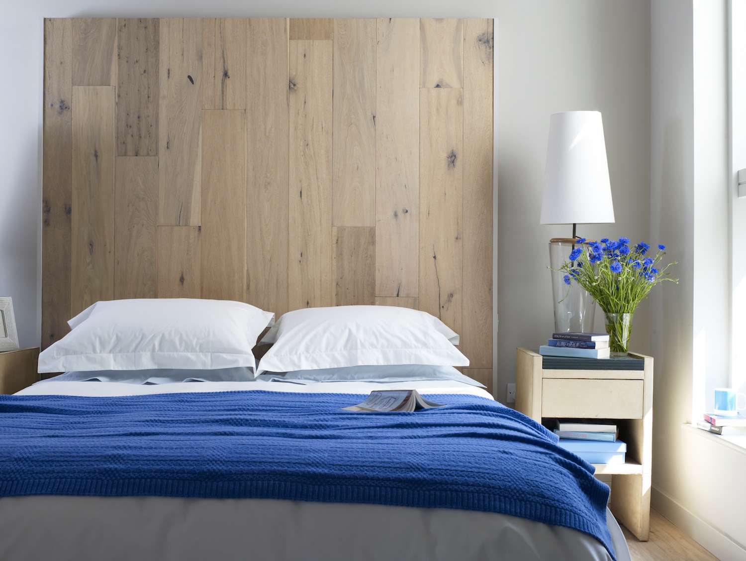 quarto com roupa de cama azul e flores azuis em um vaso em uma mesa lateral