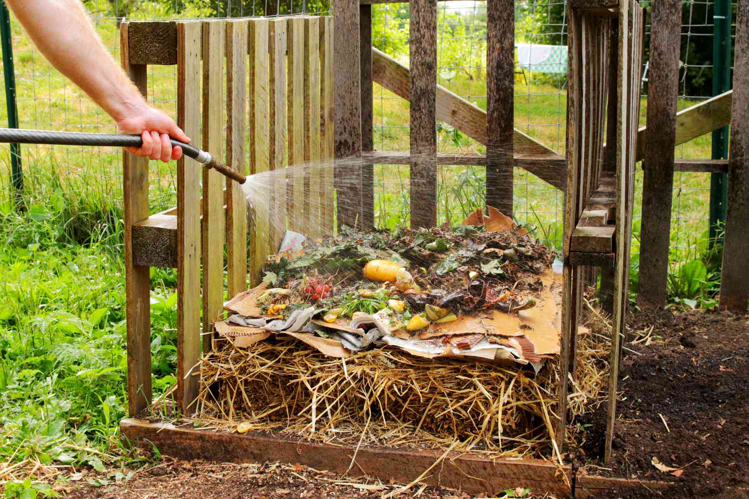 Geschichtetes, mit dem Gartenschlauch bewässertes Kompostmaterial in einem Holzbehälter