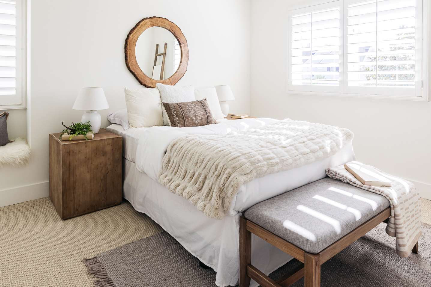 Hell erleuchtetes Schlafzimmer mit weißen und hellbraunen Decken über dem gemachten Bett