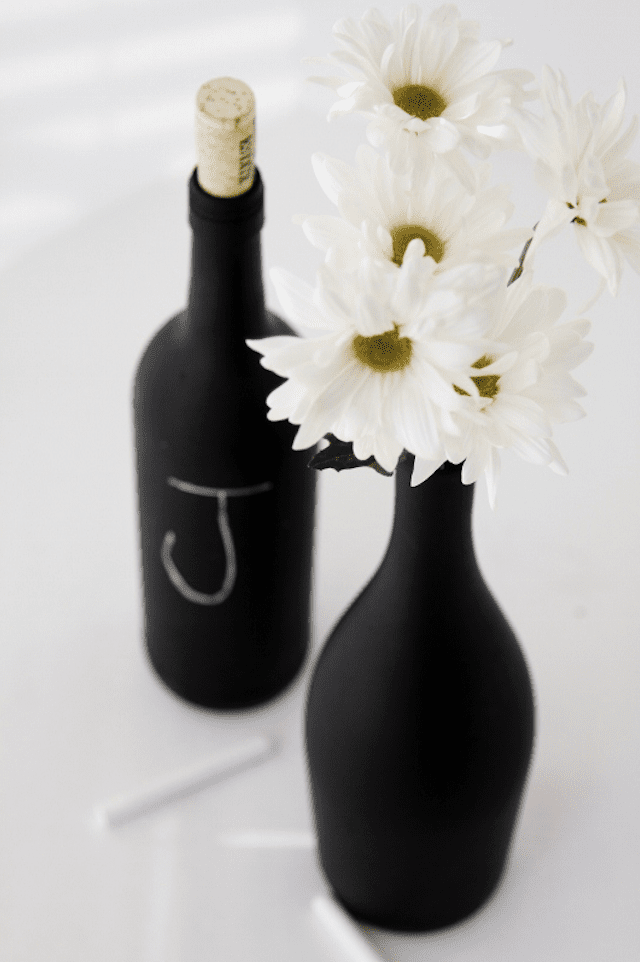 Mit Kreide bemalte Flaschen mit einem Kreidebuchstaben und Blumen darin