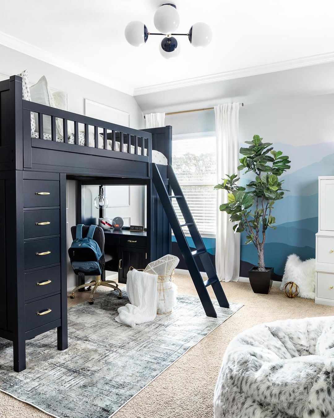 Una cama alta azul marino en la habitación de un niño con un puesto de deberes en la parte inferior y cajones en un lateral.