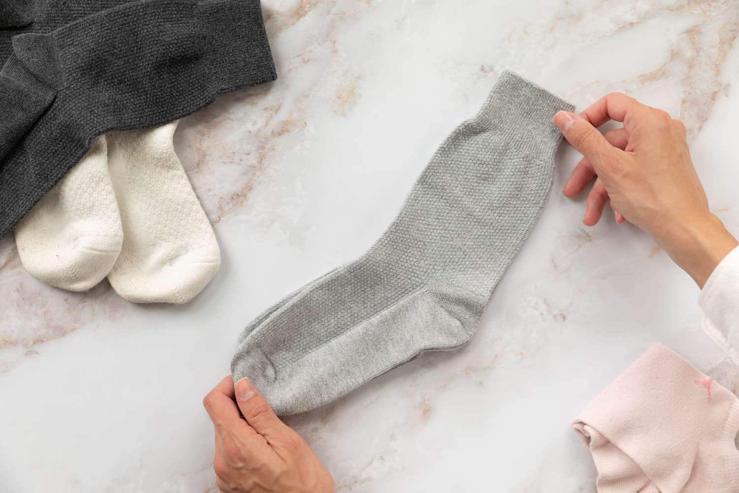 Ein Paar graue Socken, die mit der Hand an beiden Enden neben anderen Socken gehalten werden