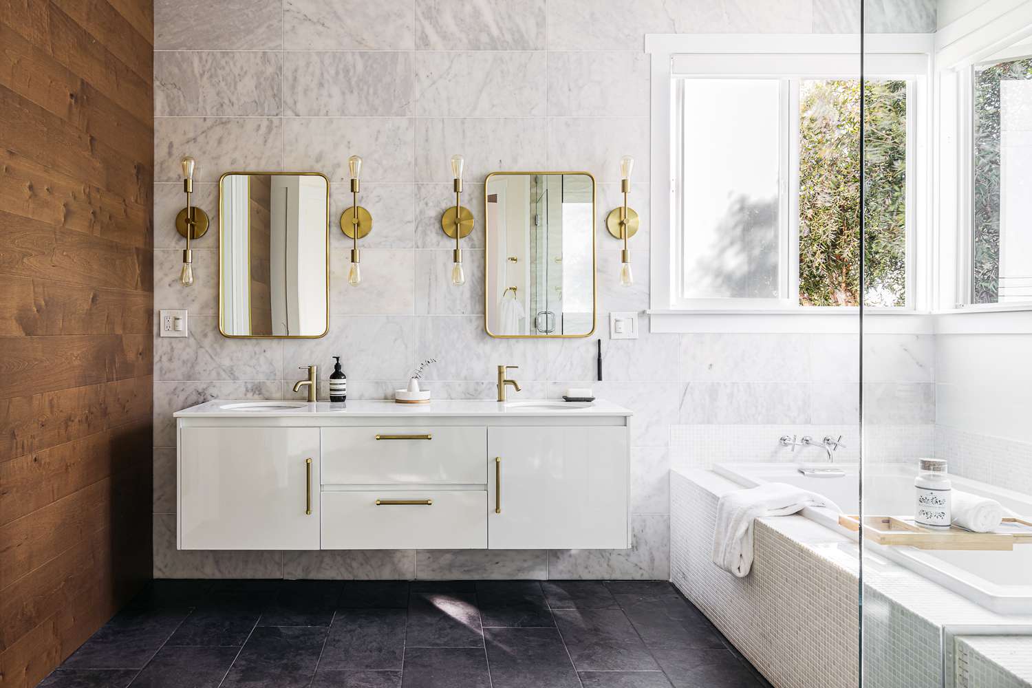 Grande salle de bain avec des luminaires décoratifs autour des miroirs et de grandes fenêtres au-dessus de la baignoire