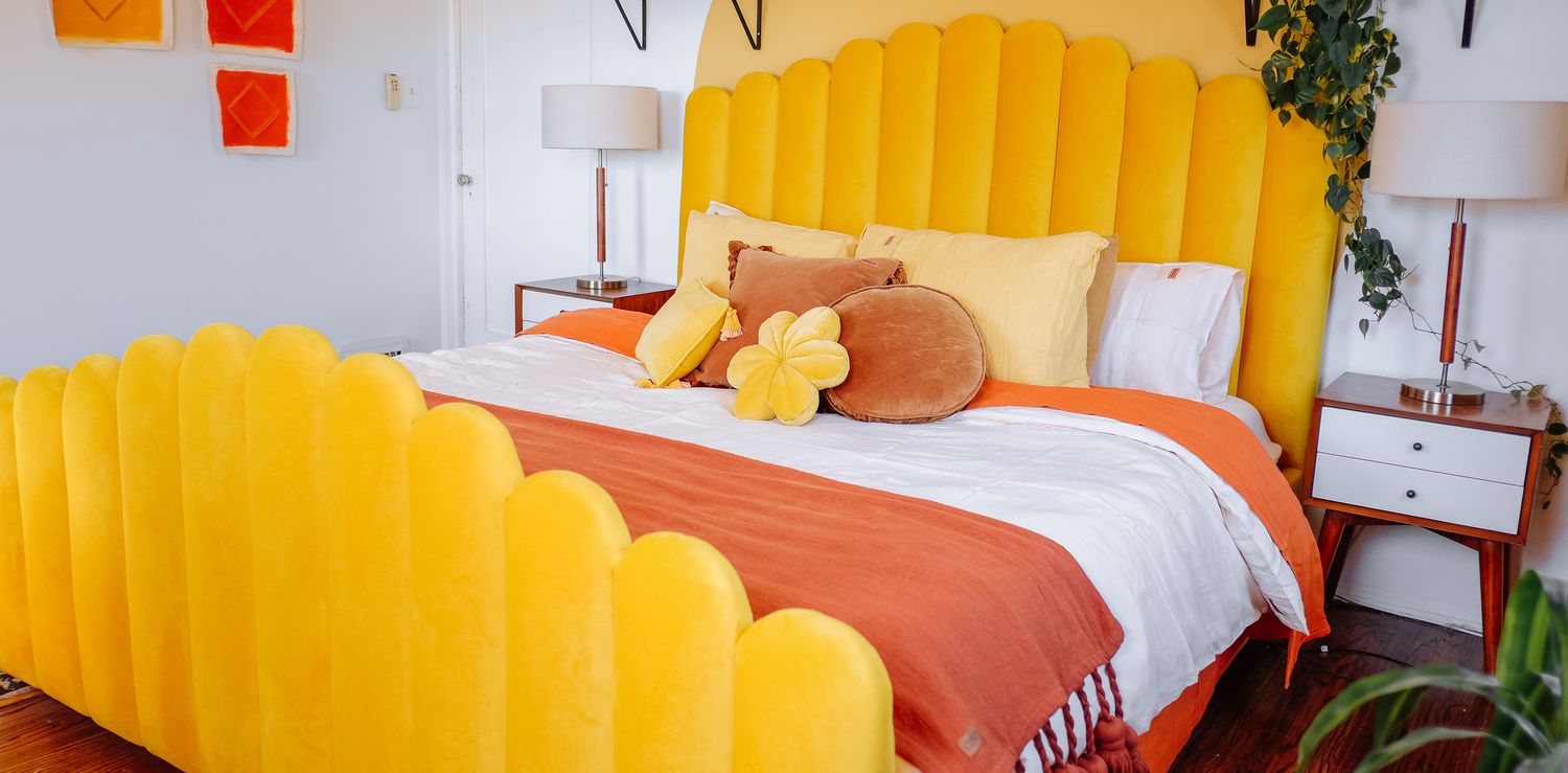 bedroom with pelh yellow headboard, yellow mural, orange blankets