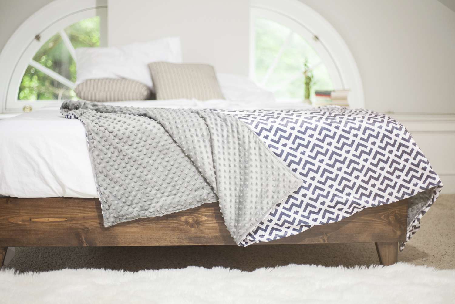Cobertor ponderado reversível em uma cama com estrutura de madeira e lençóis brancos
