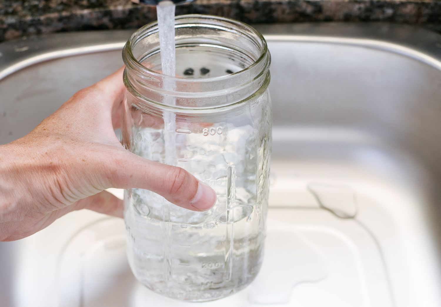 Frasco de cristal llenándose de agua en el fregadero de la cocina