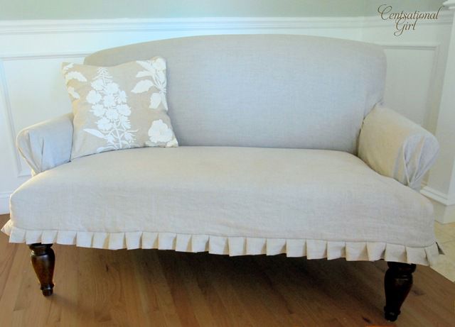 Un sofá de color claro con patas marrón oscuro y un cojín floral.