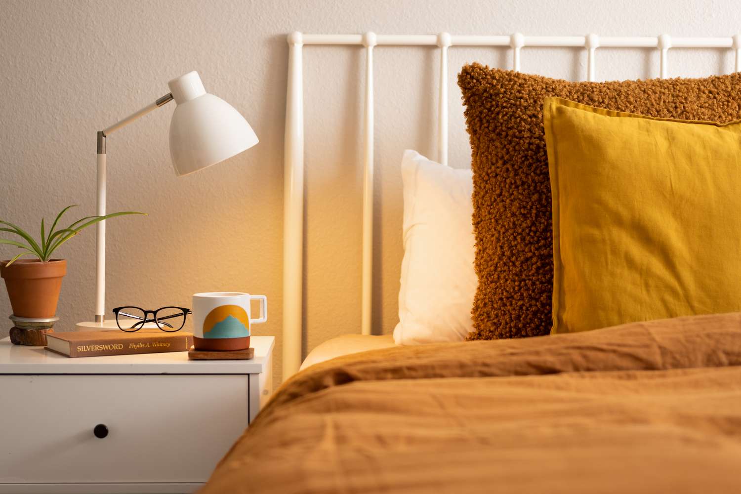 Weiße Tischplatte in warmem Licht auf Nachttisch und Bett mit brauner Bettwäsche