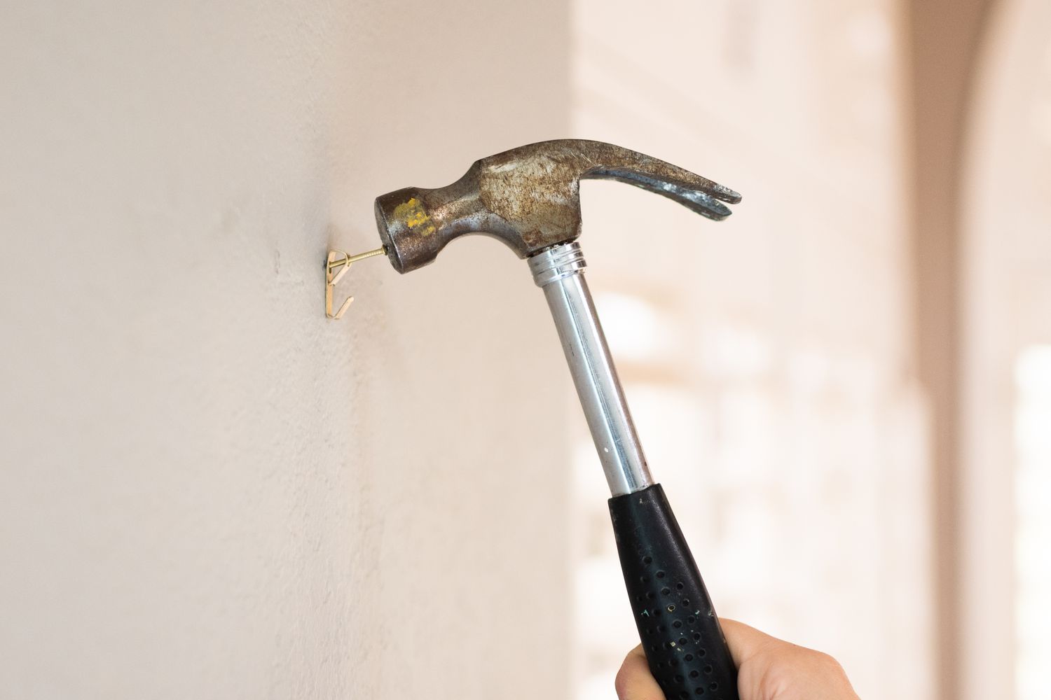 Hammer, der den Nagel an die Wand schlägt, um die Unterseite des Sägezahnaufhängers zu befestigen