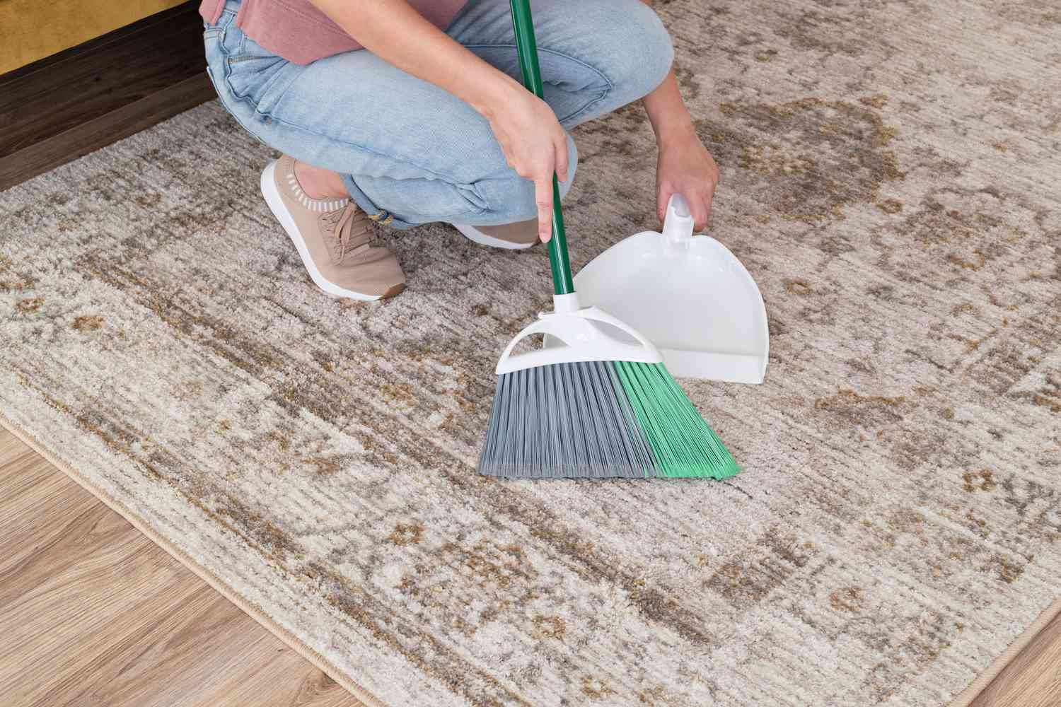Person using a broom and dustpan to clean and area rug mess