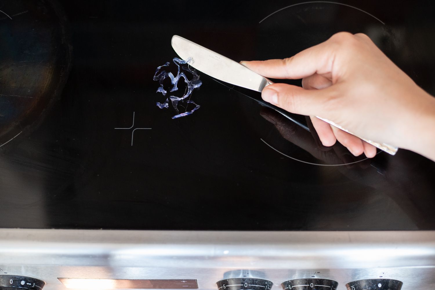 Geschmolzenes Plastik mit einem stumpfen Messer vom Glas-Kochfeld geschabt