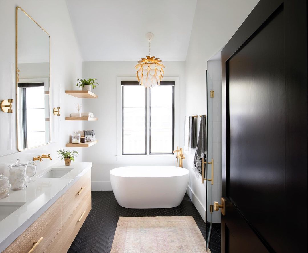 Ein Badezimmer mit schwarzen Bodenfliesen und einem goldenen Kronleuchter über der freistehenden Badewanne