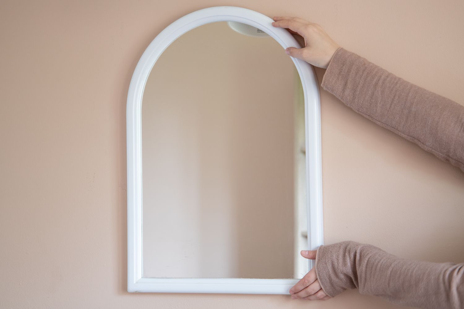 Espelho com moldura branca sendo colocado na parede
