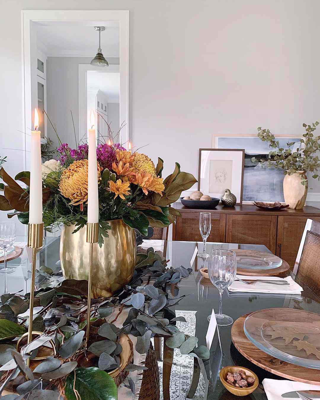 Mesa posta com flores laranja e roxas, eucalipto e castiçais dourados com velas brancas