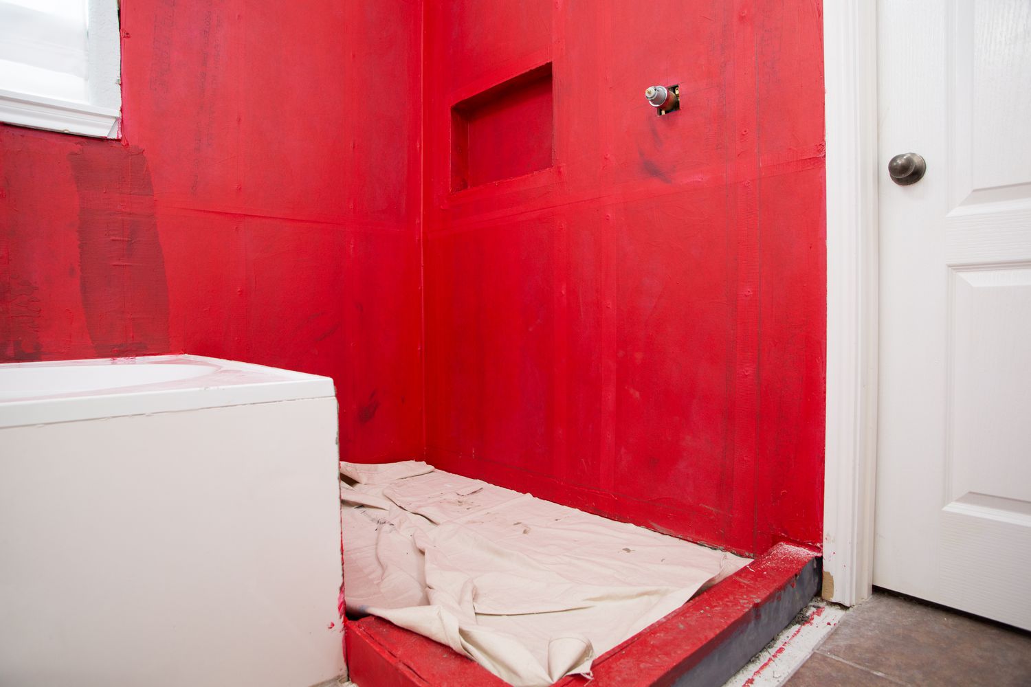 Surface du sol recouverte de tissu blanc dans une salle de bain aux murs rouges avant la pose de carreaux de céramique