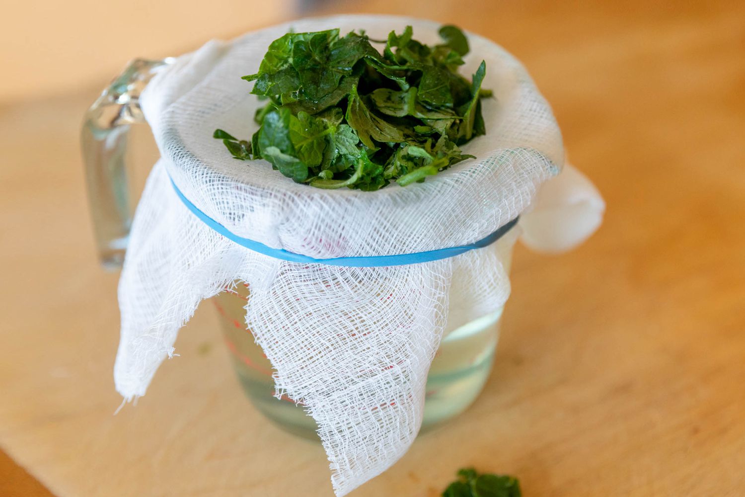 Feuchte Tomatenblätter durch ein Käsetuch in einer Tasse Wasser gesiebt