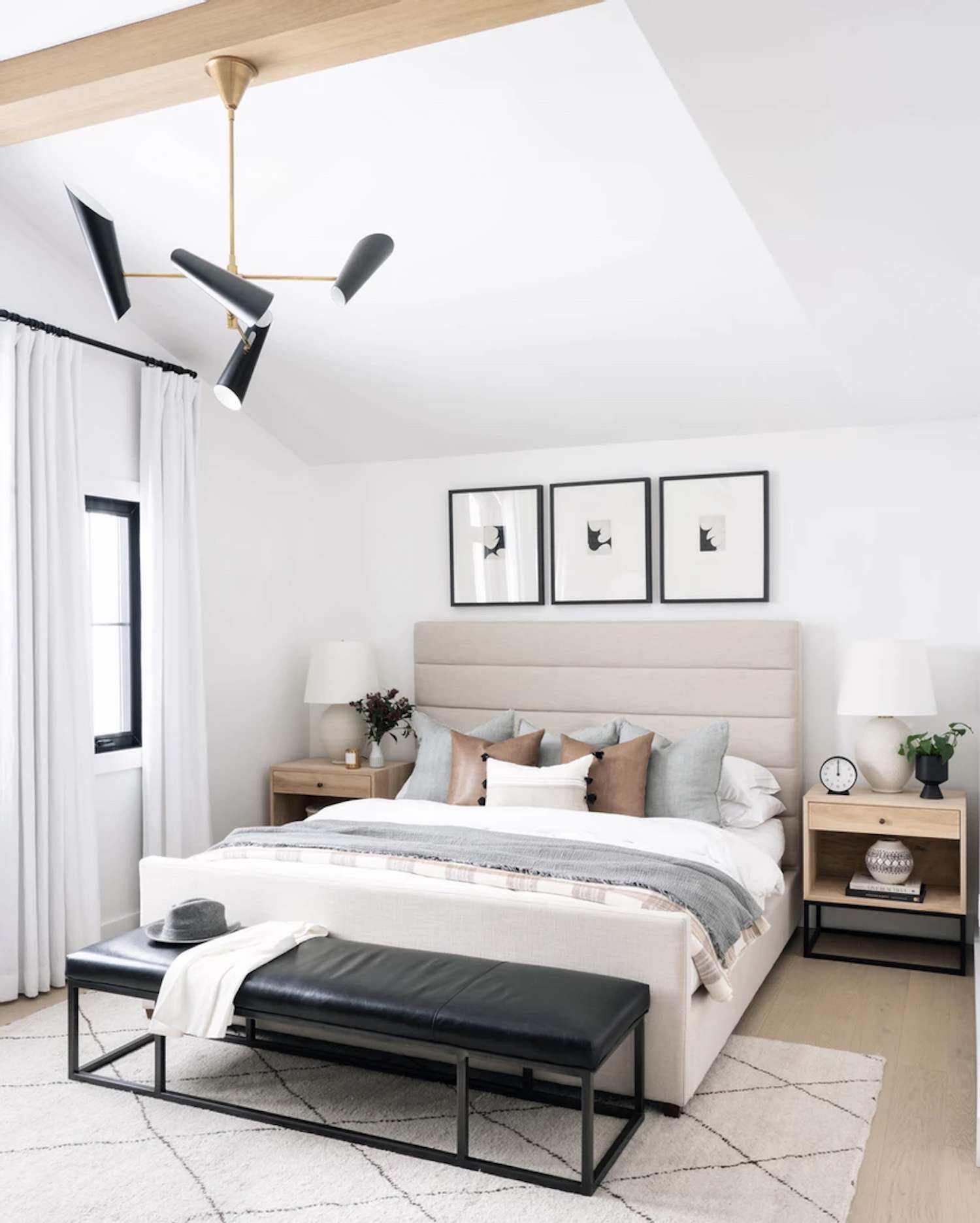 dormitorio moderno con detalles en gris claro y marrón. alfombra de área blanca. Banco de cuero negro al final de la cama