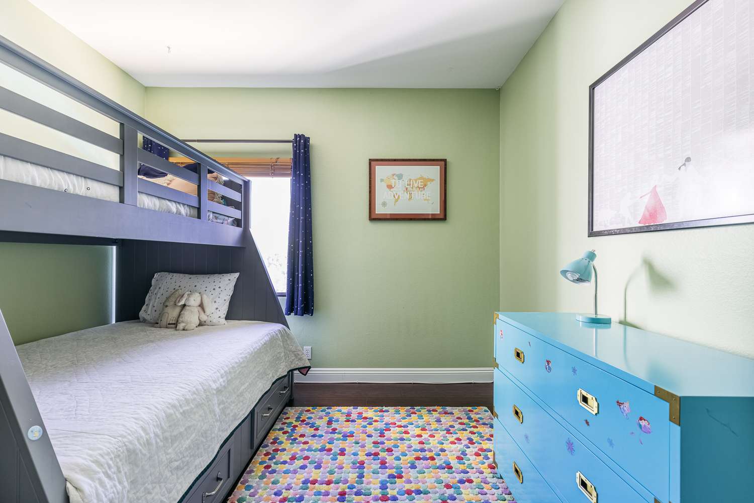 Twin bunkbed with blue railings across royal blue dresser and colorful patterned rug in middle