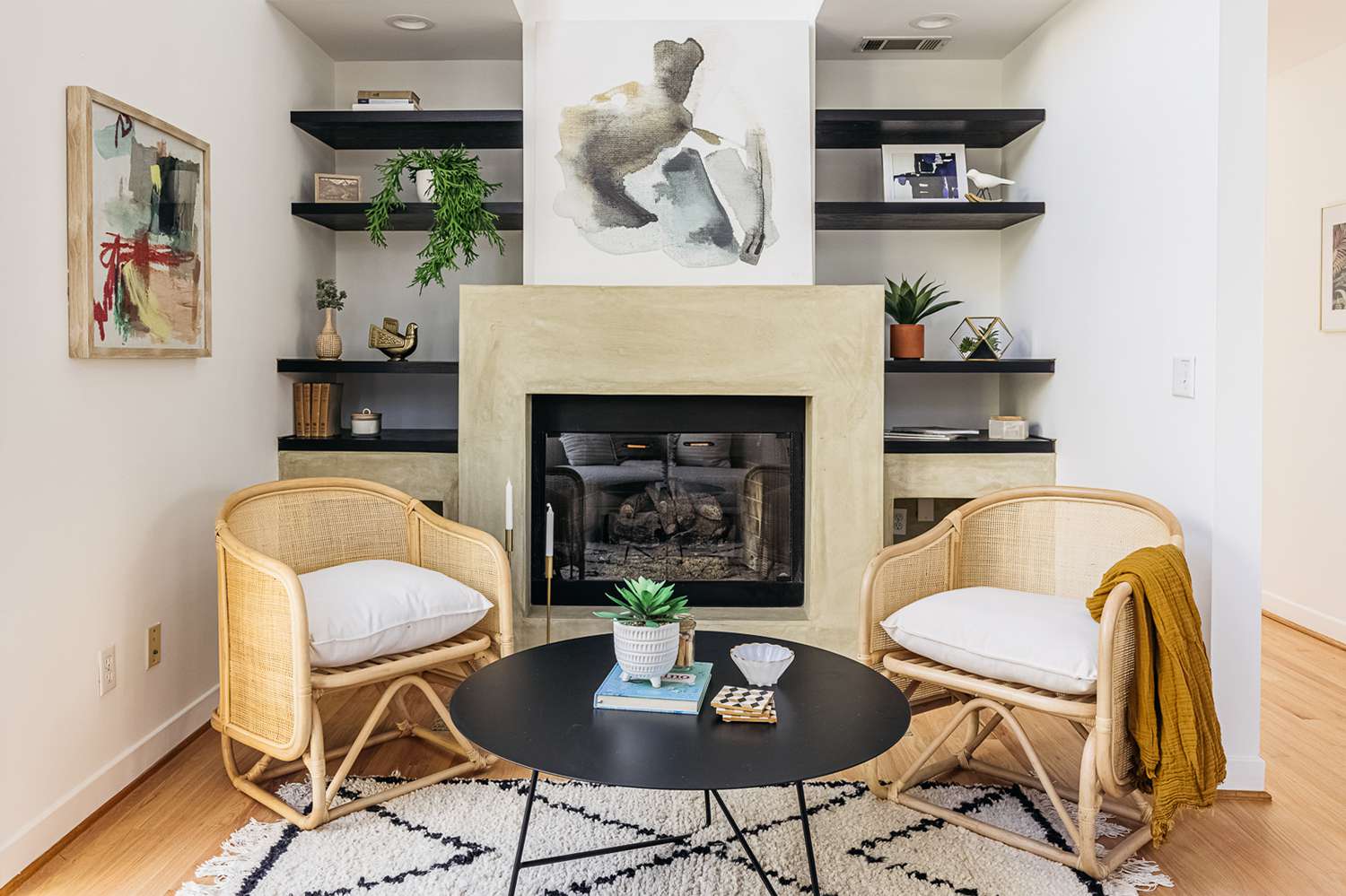 Modern tan fireplace flanked by floor to ceiling open book shelves with two wicker chairs in front