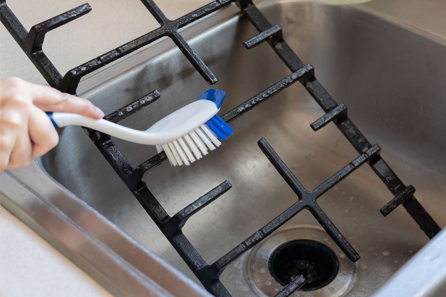 Escova de nylon com cerdas duras limpando as grelhas do fogão de ferro fundido