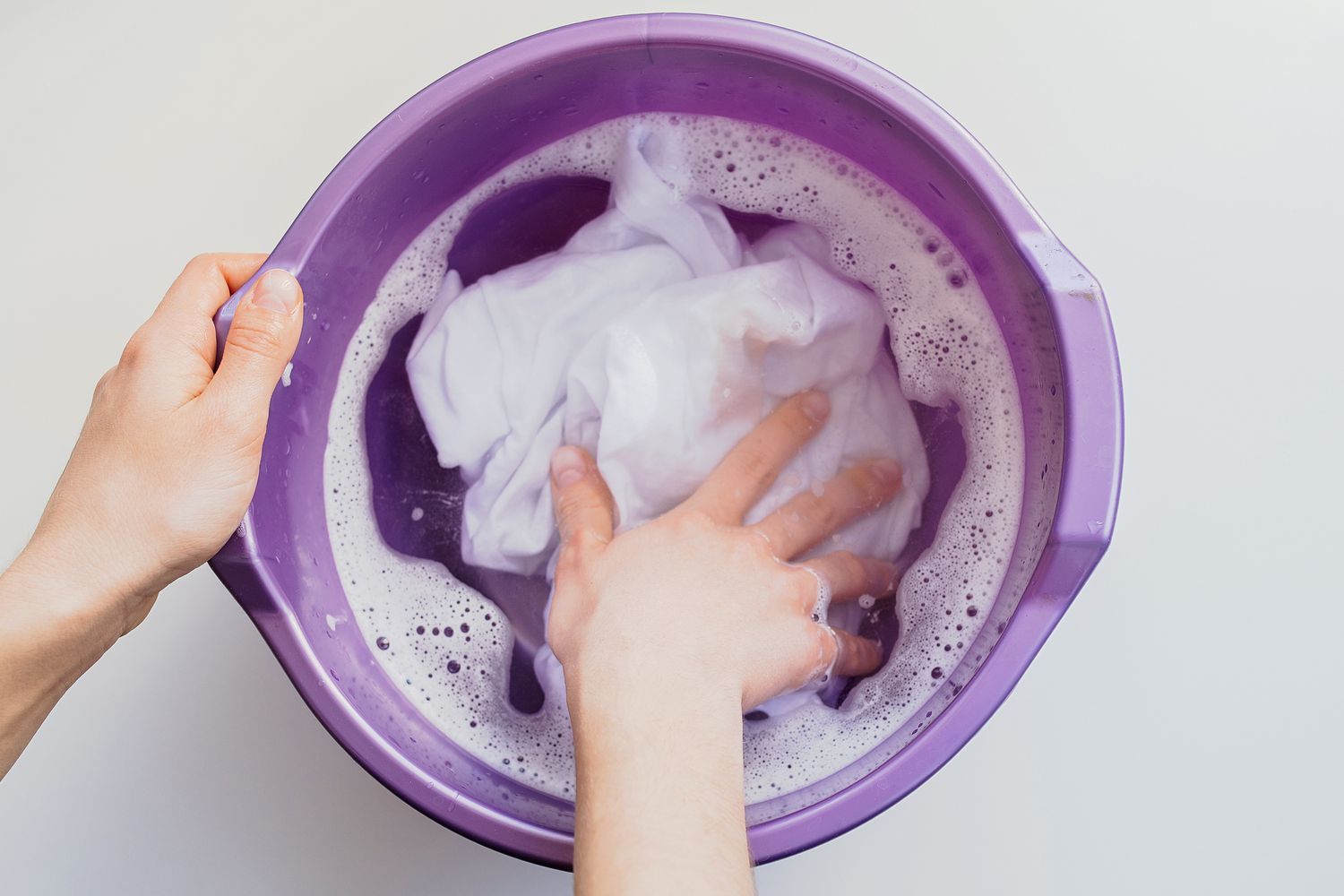Chemise blanche trempée dans un seau violet avec de l'eau chaude et de la lessive liquide