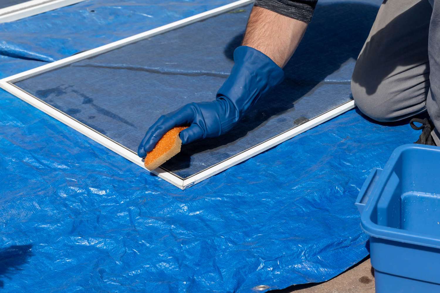 Fensterscheibe wird mit Schwamm auf blauer Plane gereinigt