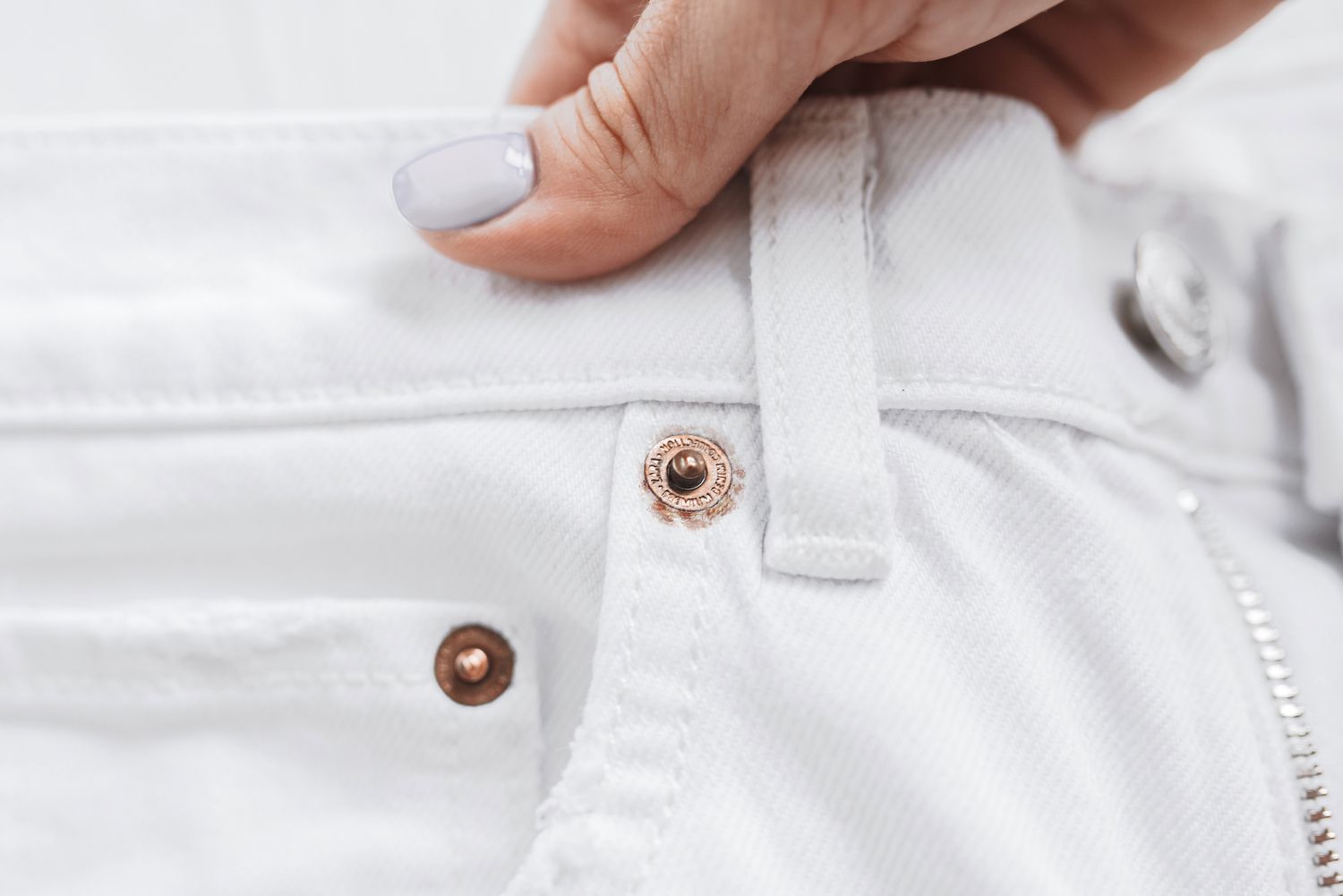 Roségoldene Metallverzierung an der Gürtelschlaufe einer weißen Jeans