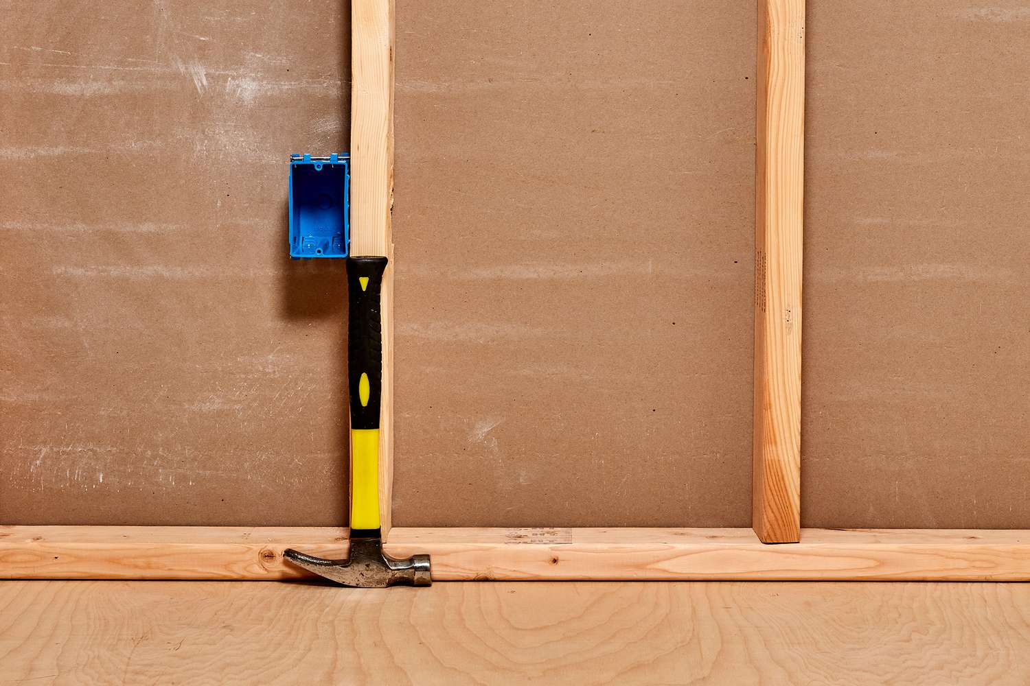 Gelber und schwarzer Hammer, der gegen einen Holzbalken gelehnt wird, um die Höhe der Wandsteckdose oder des Schaltkastens zu bestimmen