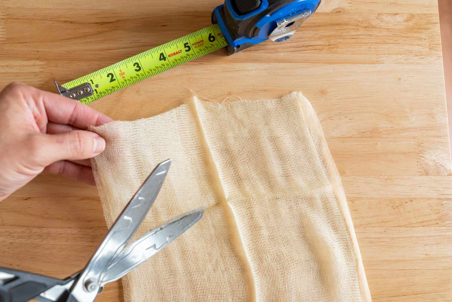 Tack cloth sendo cortado com uma tesoura ao lado de uma fita métrica