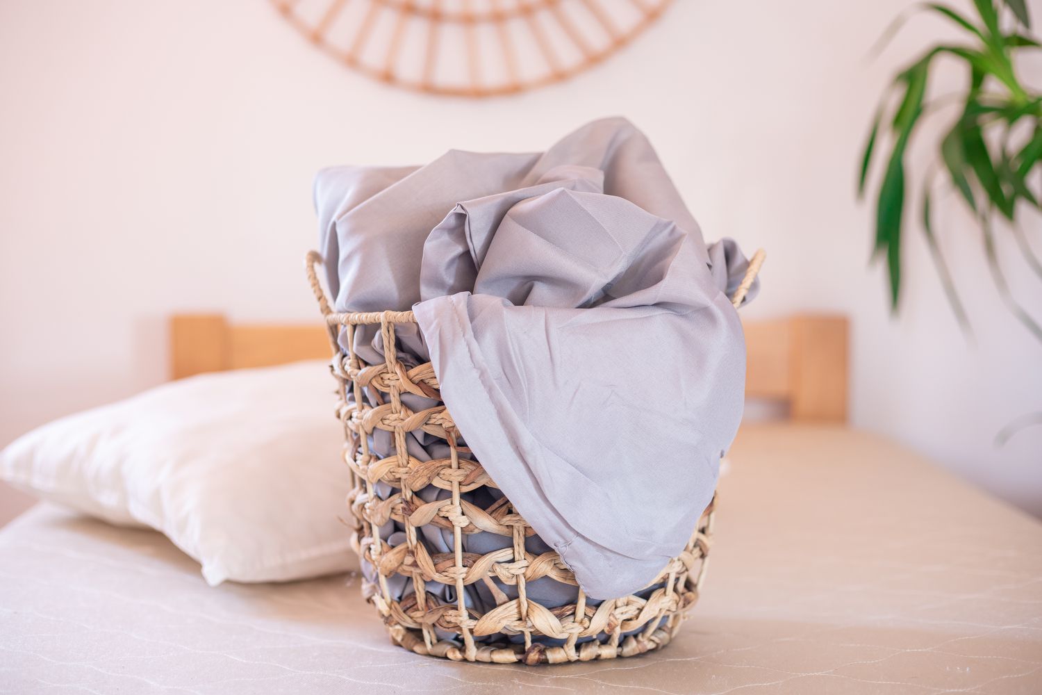Hellgraue Bambuslaken in einem geflochtenen Korb auf einem kahlen Bett