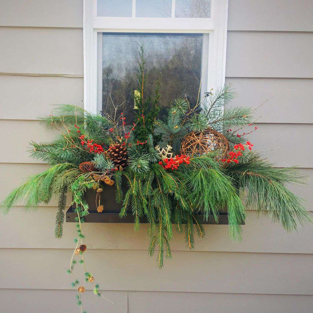 Blumenkasten am grauen Haus mit drapierten immergrünen Zweigen, Tannenzapfen, Weidenkugeln und roten Beeren