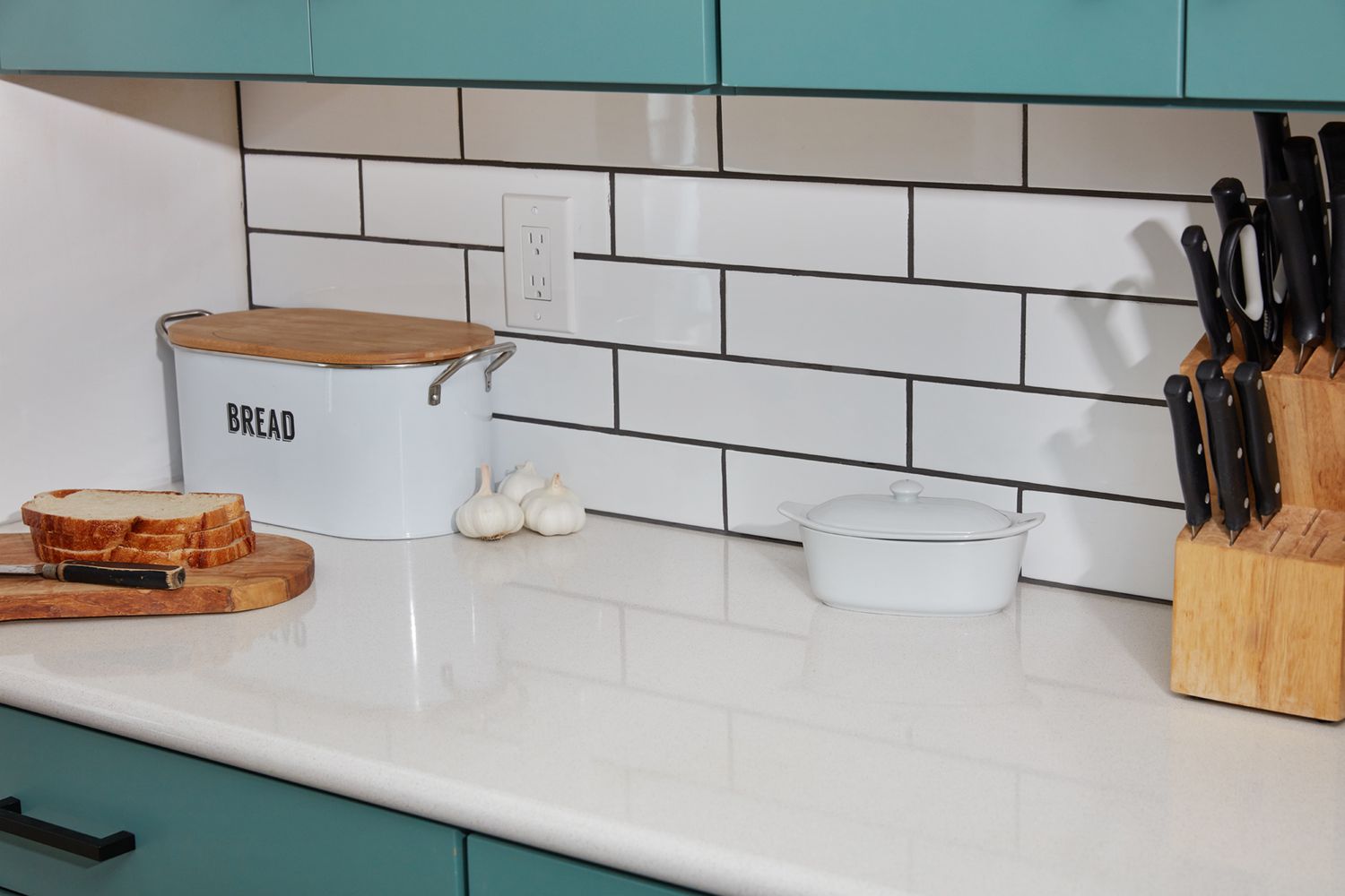 Azulejos brancos de cozinha usados como backsplash ao lado da caixa de pão, do recipiente de manteiga e das facas