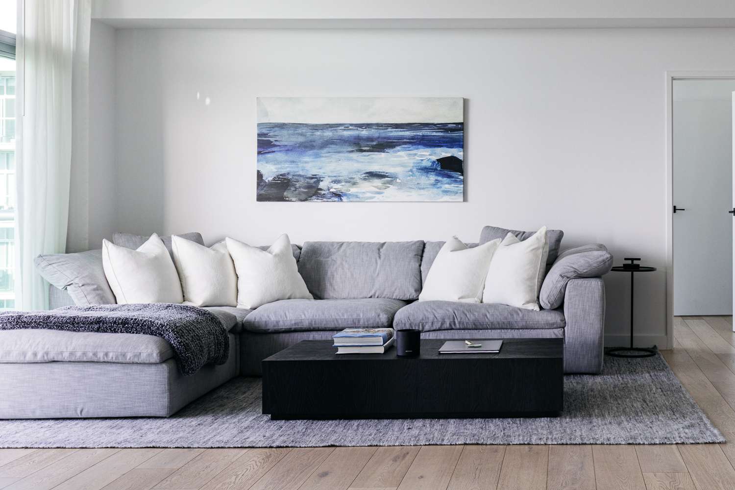 Hellgraue Sektionscouch mit weißen Kissen im minimalistisch eingerichteten Wohnzimmer